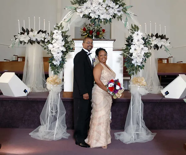 Couple posing under floral arch at church wedding ceremony- SJRIMAGES