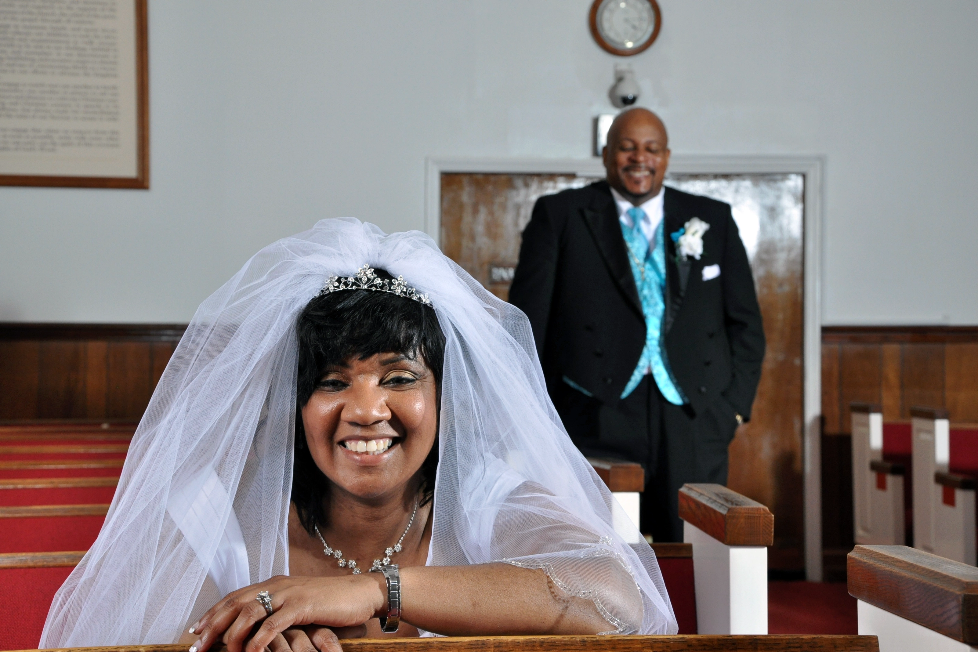 Smiling bride in pew with groom in background at church- SJRIMAGES